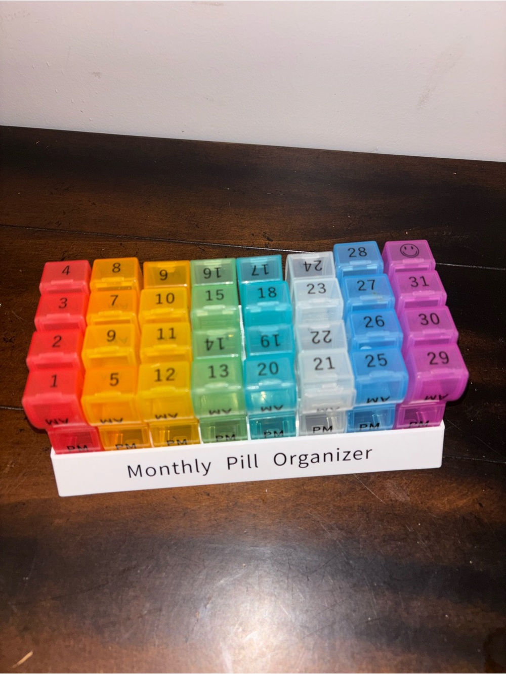 Rainbow-colored monthly pill organizer featuring 32 numbered compartments